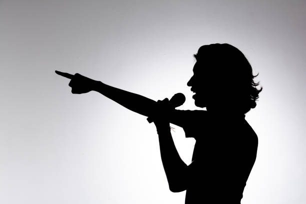 istock Silhouette of young man holding wireless microphone and pointing forward. 2160804851