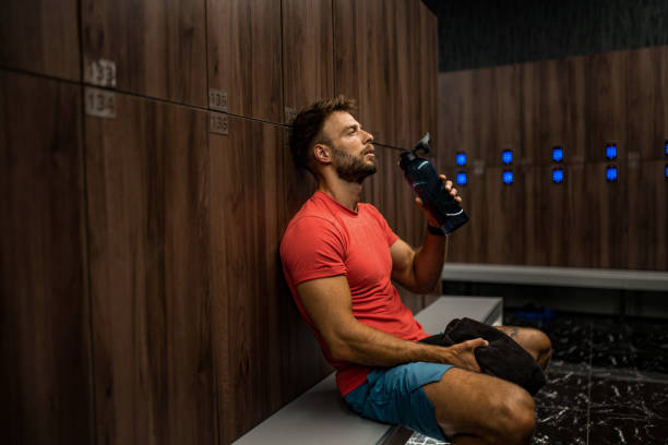 istock Tired athletic man drinking water and resting in locker room. 2160806846