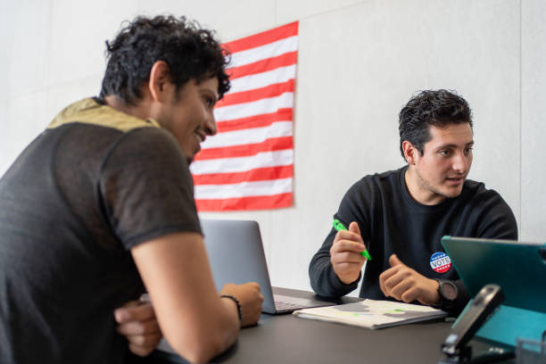 istock hispanic man register for vote, the polling worker giving a vote button, register queue for election in us 2160818142