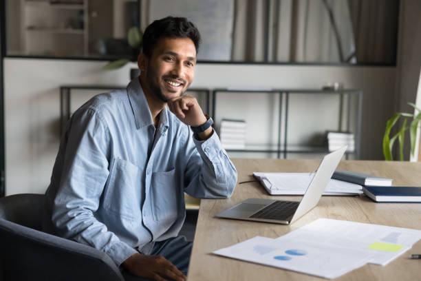 istock Cheerful young Indian business man sitting at workplace 2160820119