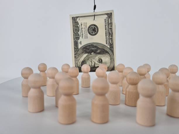 istock Wooden Figures Surrounding A Hanging One Hundred Dollar Bill 2160823850