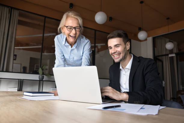 istock Cheerful younger and elder project coworkers using laptop for work 2160824892