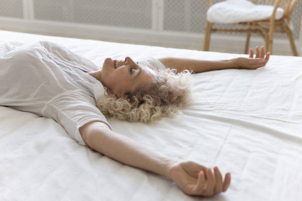 Smiling mature woman falling down on fresh bedsheets, close up