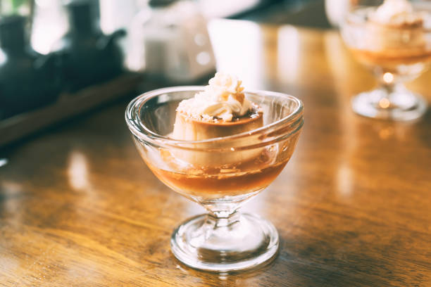 Custard vanilla pudding topping with cream and caramel. In glass cup place on wooden table in Japanese style cafe.
