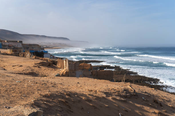 istock Poor Moroccan fishing village, Atlantic Ocean shore, Simple structures and sandy terrain, waves crashing on coastline 2160841928