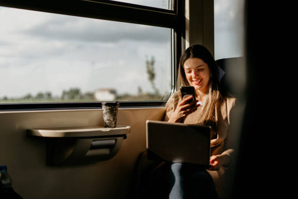 young woman travels by train, using lap top and mobile phone