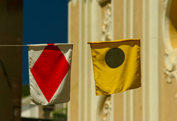A red warning flag flutters in the wind against a clear sky with the sun low on the horizon, casting a glow around the flagpole. A lone bird glides across the open sky, adding a sense of stillness and vastness to the scene.