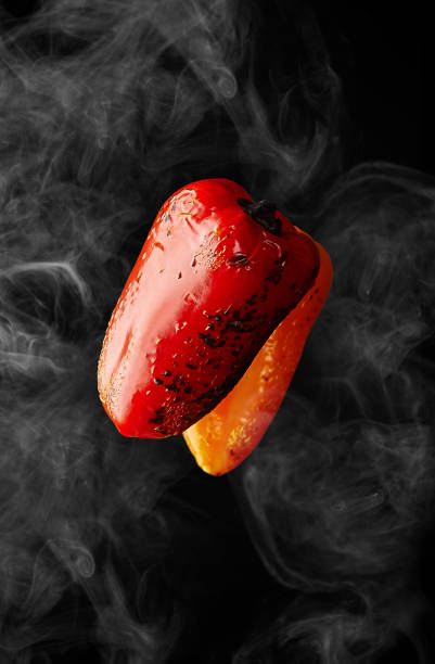Closeup of hot grilled red and orange bell peppers hovering in white haze on black background. Vertical image