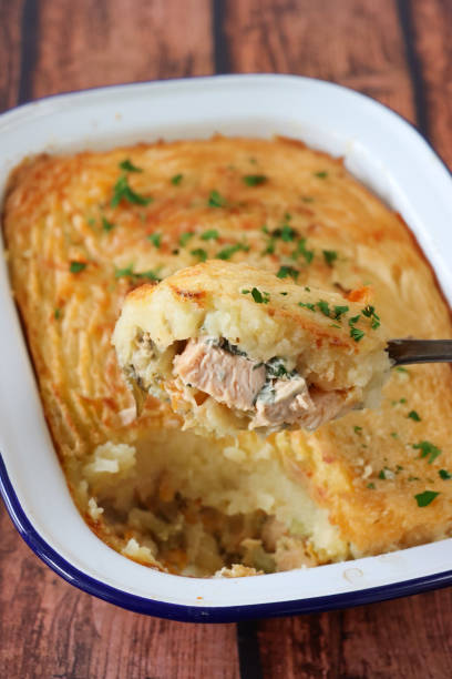 istock Close-up image of spoonful of cooked, homemade fish pie, missing portion displaying salmon, cod and smoked haddock chunks, grated carrots, leeks, red chilli in enamel ovenproof dish, crispy golden, mashed potato topping with forked pattern, elevated view 2160847298