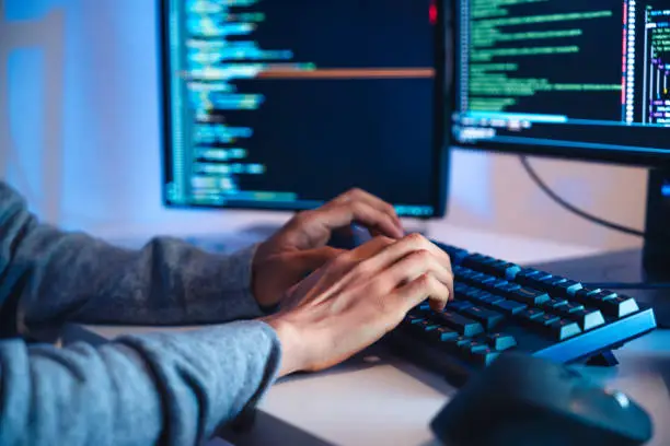 Photo of close up hand of Asian prompt engineer develop coding app with software data sitting in front of computer monitor at office