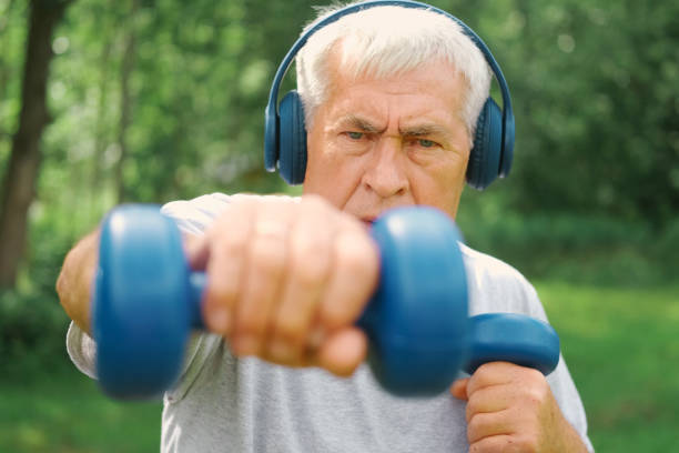 istock Old man exercising with dumbbells outside. Physical therapy. Elderly 60s male working out. Active sporty gray haired man standing with weights. Older person doing fitness outdoors. People, gym, sport 2160851948
