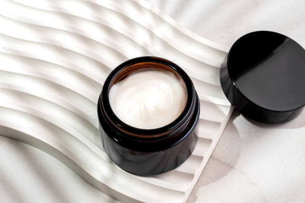 istock Open Cosmetic cream jar with palm leaf shadow on light concrete podium on marble background. Dermatologic, components for cosmetics. 2160854079
