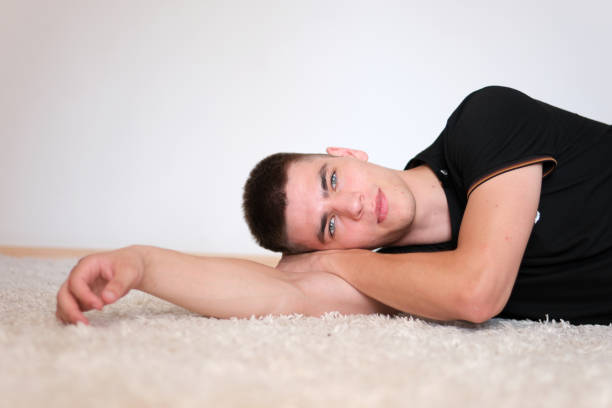 Handsome man with black hair and blue eyes. Mixed race nationality. guy put his head on his hand lying on a white carpet resting relaxation
