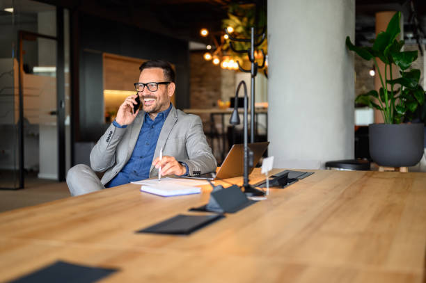 istock Handsome entrepreneur discussing over mobile phone while working on project at desk in modern office 2160857049