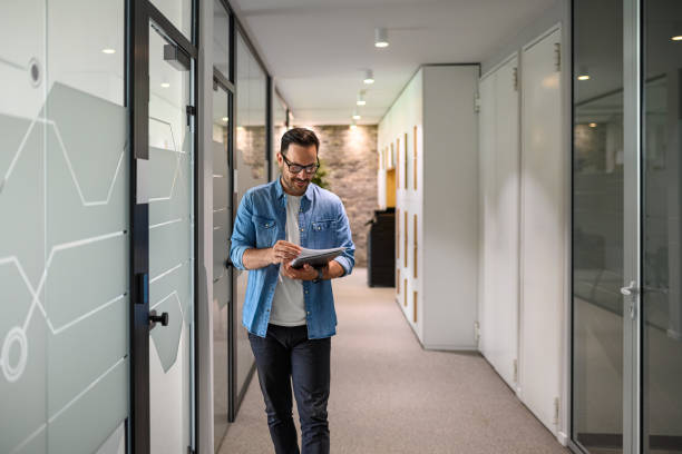 istock Smiling male financial advisor in eyeglasses analyzing reports while walking in office corridor 2160857104