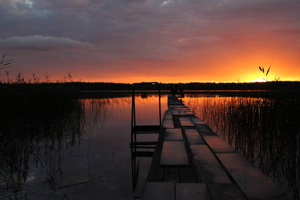 Epic red and golden clouds above the forest lake at sunset. Dramatic cloudscape. Symmetry reflections on the water, natural mirror. Idyllic rural scene.