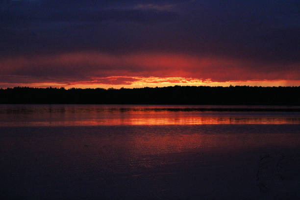Epic red and golden clouds above the forest lake at sunset. Dramatic cloudscape. Symmetry reflections on the water, natural mirror. Idyllic rural scene.