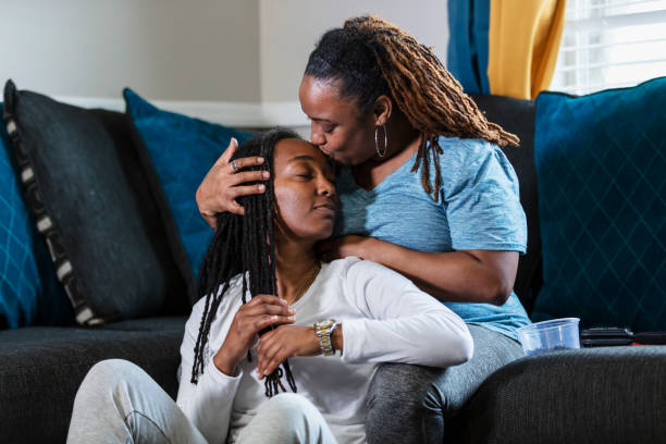 African-American lesbian couple, kiss on forehead An African-American lesbian couple sitting together at home. Their eyes are close as one of the women kisses her partner on the forehead. lesbian couple embracing stock pictures, royalty-free photos & images