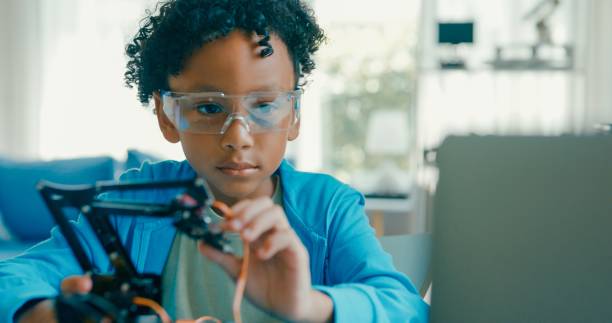 istock Young African-American boy explores robotics and engineering at home, demonstrating enthusiasm and focus during an online educational session. STEM Education robotics courses online. 2160910147