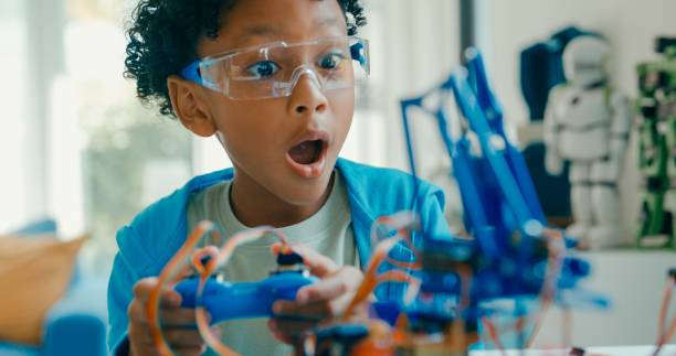 Closeup of Young African-American boy using remote control for robotics project amidst various technological tools and models at home. STEM Education robotics courses online.