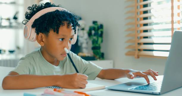 istock Young African-American boy wearing headphones, is deeply focused while participating in online learning session from home. Education courses online. 2160910201