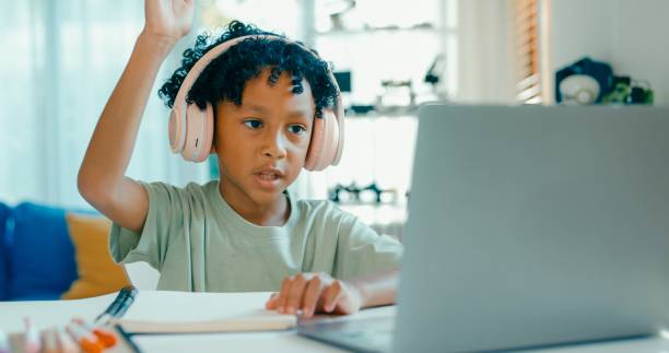 istock Young African-American boy wearing headphones, is deeply focused while participating in online learning session from home. Education courses online. 2160910202