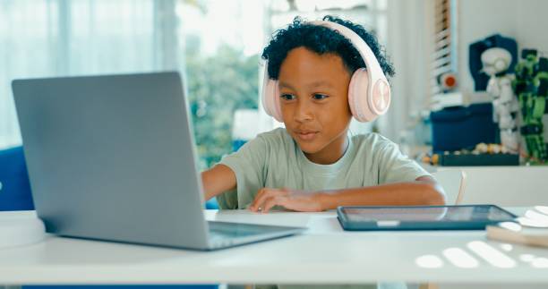 istock Enthusiastic young African-American boy interacts with online class using laptop and digital tablet, fully absorbed in educational activities at home. Education courses online. 2160910228