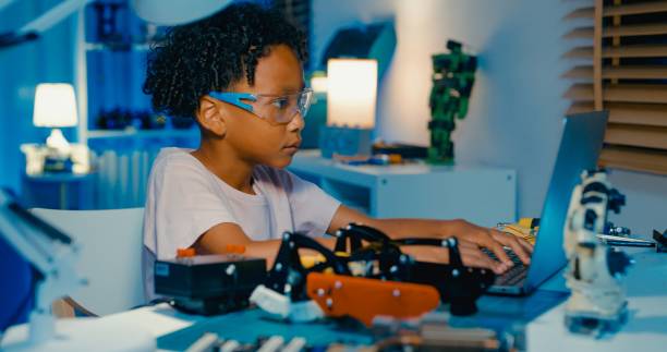young african-american boy learning programming codes on laptop while building and programming robotics in home at night. stem education robotics courses online. - redactioneel stockfoto's en -beelden