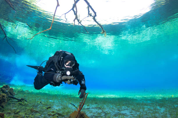 A diver using a rebreather is diving in a crystal clear water surrounded by beautiful water and nature