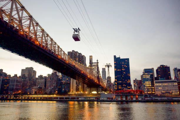 The Queensboro Bridge at Golden Hour while the Roosevelt Island Tram heads across on its cables over the East River with the Manhattan skyline in the background