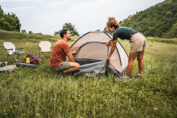 boyfriend and girlfriend set up a tent in nature ready for camping