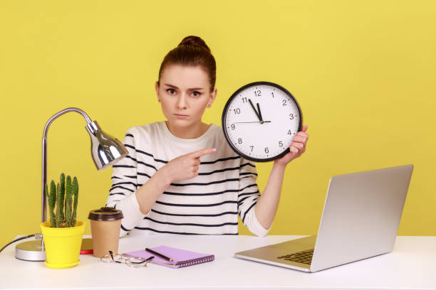 istock Woman pointing finger at big wall clock, time management, looking at camera with strict expression. 2160938317