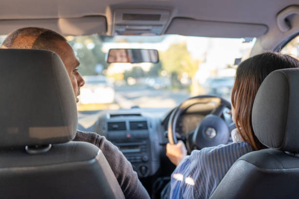 A teenage girl sits behind drivers wheel and has lessons from a male driving instuctor