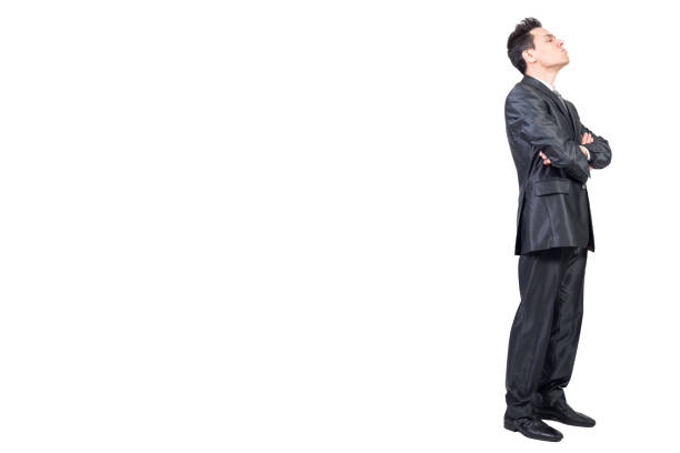 Full body side view of arrogant male entrepreneur wearing formal suit standing with crossed hands and closed eyes on white isolated background