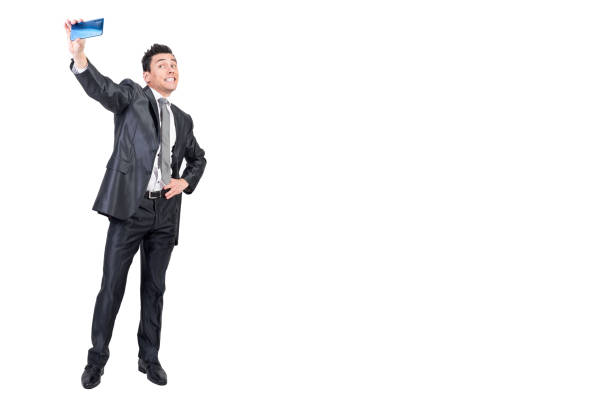 Comic male entrepreneur wearing classy suit taking self shot on mobile phone against white isolated background