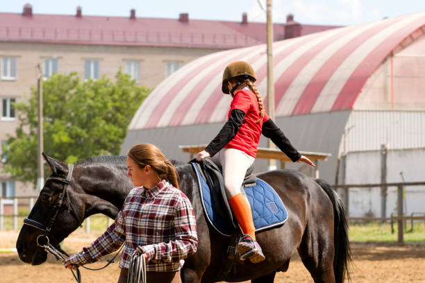Instructor assists young rider during outdoor equestrian session. Riding school