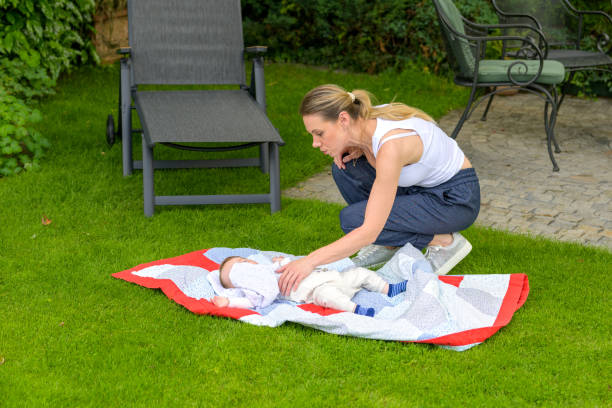 A mother checks on her baby who is sleeping on a quilt in the garden.