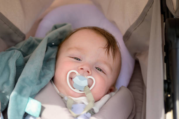 Close up of a baby with a pacifier lies comfortably in a stroller, enjoying a sunny day outdoors
