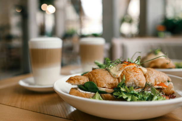 croissant sandwiches and coffee cups on wooden table.