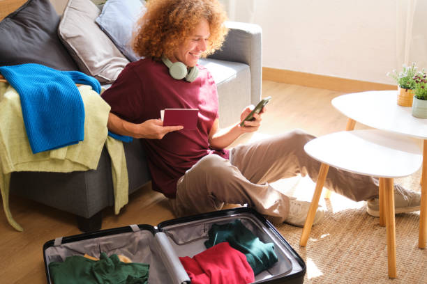 istock Smiling young man holding passport using smartphone near packed suitcase 2160982952