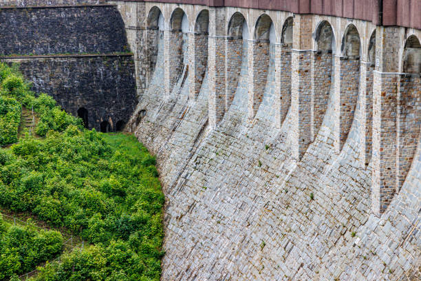 Huge wall with parapet, arches, buttress and pillars at Robertville Dam, green trees and wild vegetation in background, cloudy day in Waimes, Belgium
