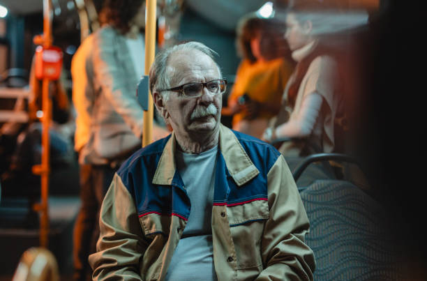 An elderly man with glasses and mustache sitting on a bus during a city commute.