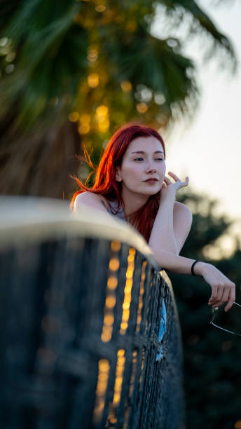 A serene portrait of a woman captured in soft, golden light as the sun sets. The backlit composition highlights her delicate profile and gently tousled hair, evoking a sense of calm and reflection. The warm sunlight creates a dreamy, ethereal atmosphere, with a subtle bokeh effect in the background. This image beautifully captures the quiet moments of contemplation and grace.