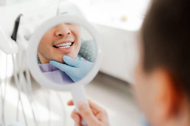 istock Smiling attractive young man, patient holding mirror looking at teeth, treatment in modern dentistry 2160992837