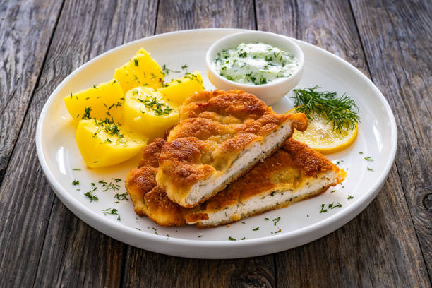 istock Crispy breaded seared chicken cutlet with boiled potatoes and cucumbers in cream served on white plate on wooden table 2160994387