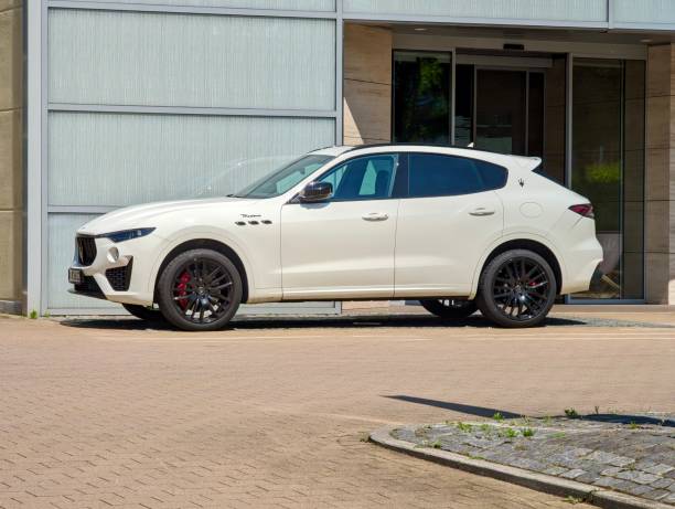 Hamburg, Germany - May 27. 2024: A white Maserati SUV parked in a public parking lot in front of a modern building with large glass windows. The image highlights the distinctive details of the vehicle, including the stylish wheels and logo, parked in the outskirts in the east of Hamburg