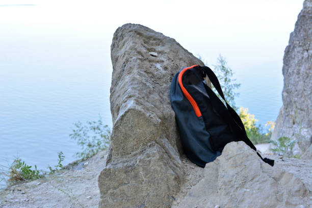 a black backpack on a rock isolated with a body of water on background