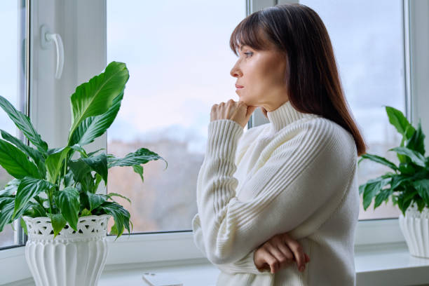 istock Serious thoughtful middle aged female looking out the window at home 2161017663