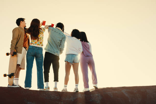 Group of friends drinking and celebrating together outdoors during sunset, enjoying a moment of camaraderie and joy.