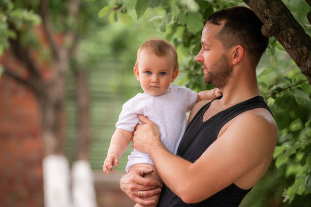 A father with a cherry tree in his hands stands under an apple tree in the garden of a country house.